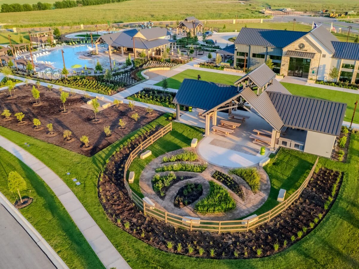 Aerial view of the Flora Market Square amenity center, showing the clubhouse, resort-style pool, covered pavilion with picnic tables, and central garden feature.